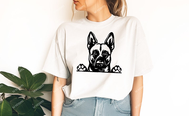 May include: A white t-shirt featuring a black and white graphic of a dog's face and paws. The dog's head is centered, with its ears perked up. The paws are at the bottom of the graphic, giving the impression the dog is peeking over.