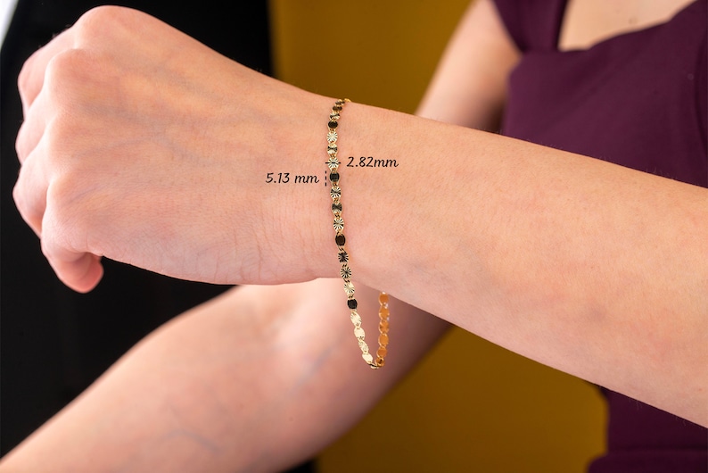 K&ouml;nnte beinhalten: Ein filigranes goldenes Armband mit kleinen, runden und ovalen Gliedern. Das Armband wird an einem Handgelenk gezeigt, mit sichtbaren Ma&szlig;en von 5,13 mm und 2,82 mm. Der Schmuck hat eine helle, gl&auml;nzende Goldfarbe.