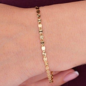 K&ouml;nnte beinhalten: Ein zartes goldenes Armband mit abwechselnd kreisf&ouml;rmigen und ovalen Gliedern. Das Armband wird am Handgelenk getragen und zeigt sein filigranes Design und subtiles Funkeln. Das Schmuckst&uuml;ck ist ein schlichtes, aber elegantes Accessoire.