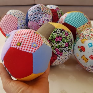Könnte beinhalten: Eine Gruppe von bunten Patchwork-Stoffbällen mit verschiedenen Mustern, darunter Blumen, Karos und geometrische Designs. Die Bälle sind aus weichem Stoff gefertigt und eignen sich perfekt für sensorisches Spiel oder als Dekorationsartikel.