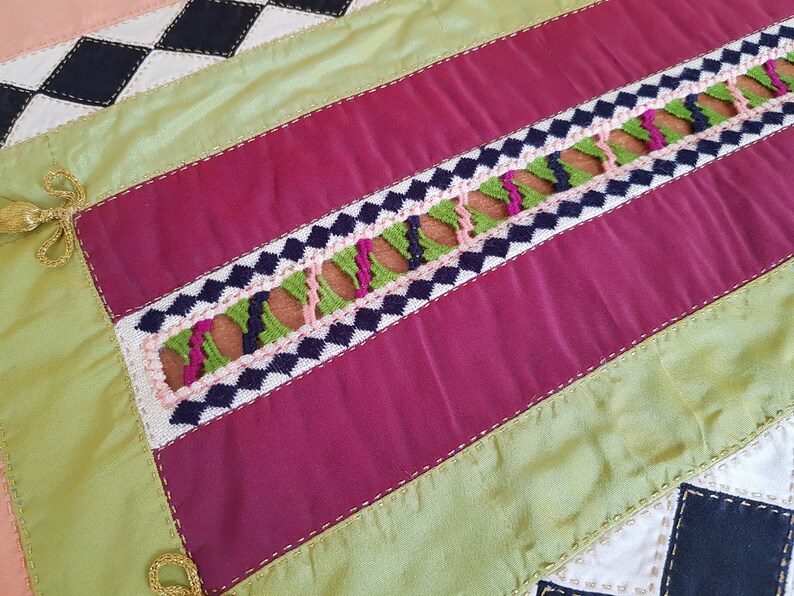 May include: A close-up of a multi-coloured fabric with a geometric pattern. The fabric is made of different shades of pink, green, black, and white. The fabric is sewn together with a decorative stitch.