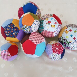 May include: Nine colorful patchwork fabric balls, each with a different pattern, including floral, geometric, and animal prints. The balls are arranged in a cluster on a white surface.