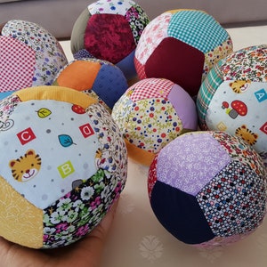 May include: A collection of eight colorful patchwork fabric balls. Each ball is made of different patterned fabrics, including floral, geometric, and alphabet prints. The balls are soft and squishy, perfect for babies and toddlers.