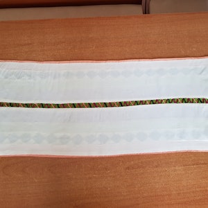 May include: White table runner with a pink border and a green, black and pink embroidered stripe down the centre.