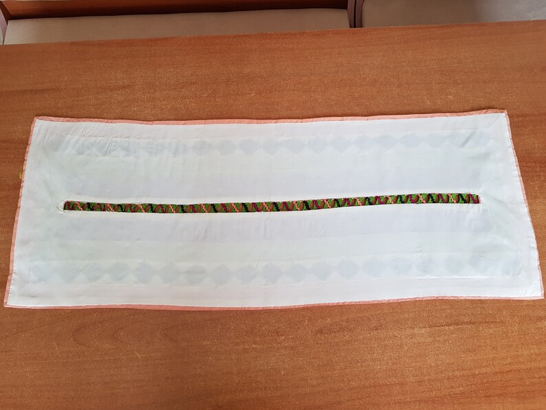 May include: White table runner with a pink border and a green, black and pink embroidered stripe down the centre.