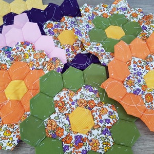 May include: A collection of handmade fabric flower appliques in various colours and patterns, including orange, yellow, green, purple, and pink. The appliques are made from floral patterned fabric and have a hexagonal shape.