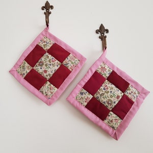 May include: Two pink and red quilted pot holders with floral patterns hanging on hooks.