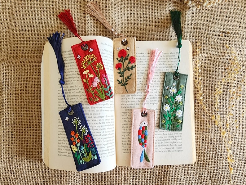 May include: Set of six embroidered bookmarks with colorful floral and fish designs. Each bookmark has a tassel and a metal ring at the top.