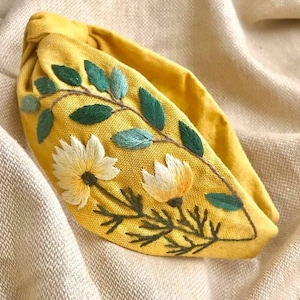 May include: A yellow fabric headband with embroidered green leaves and white flowers.
