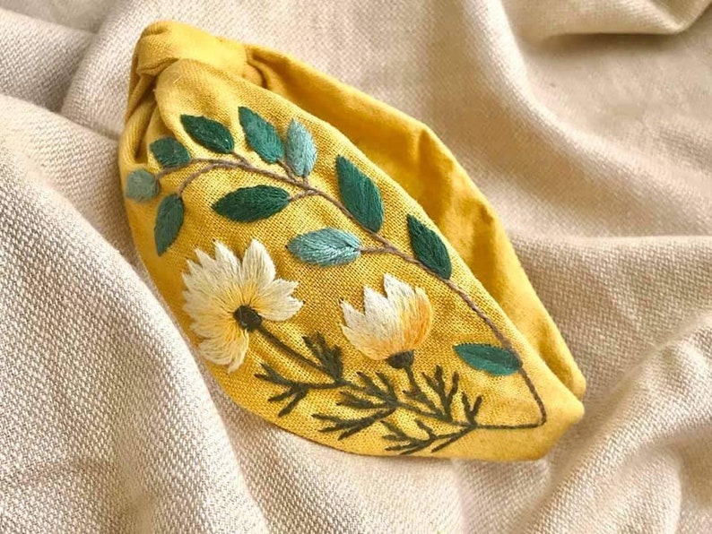 May include: A yellow fabric headband with embroidered green leaves and white flowers.