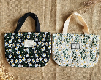 Puede incluir: Dos bolsas de mano con estampados de margaritas. Una bolsa es negra con margaritas blancas y un asa negra. La otra bolsa es blanquecina con margaritas blancas y un asa crema. Cada bolsa tiene una etiqueta rectangular que dice "PLEASANT TIME".