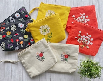 May include: A set of 7 embroidered pouches with floral designs. The pouches are made of a natural fabric and come in a variety of colors, including black, white, yellow, and red. The pouches are perfect for storing small items like jewelry, makeup, or keys.