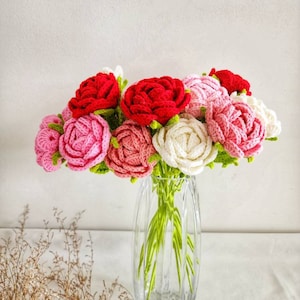 May include: A bouquet of crocheted roses in pink, white, and red colors arranged in a clear glass vase. The roses are made with yarn and have a realistic appearance.