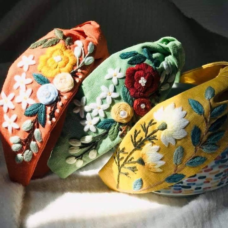May include: Three fabric headbands with floral embroidery. The headbands are in shades of orange, green, and yellow. Each headband features a different floral design.