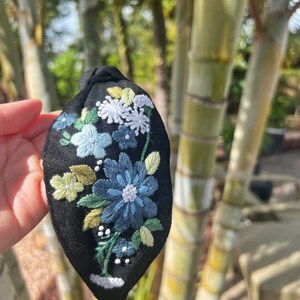 May include: Black fabric headband with embroidered flowers in shades of blue, green, and white.