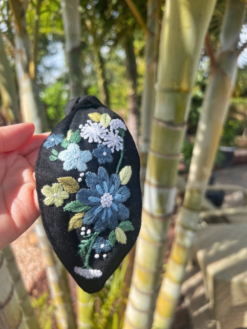 May include: Black fabric headband with embroidered flowers in shades of blue, green, and white.