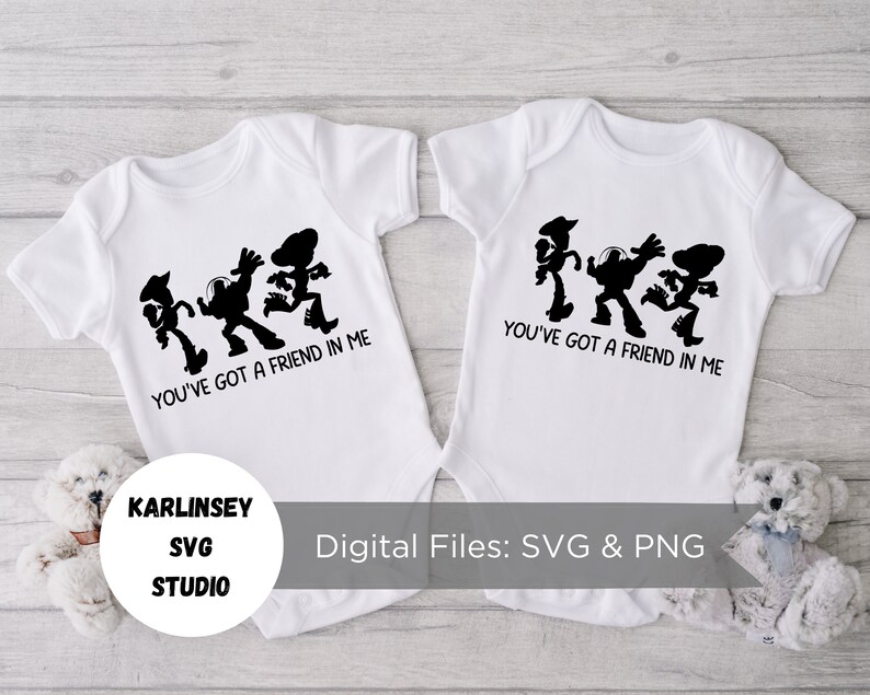 Op de afbeelding: Twee witte baby-rompers met zwarte silhouetten van Woody, Buzz Lightyear en de alien uit Toy Story. De rompers hebben de tekst "You've got a friend in me" erop gedrukt.