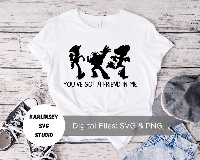 Op de afbeelding: Wit T-shirt met een zwart silhouet van Woody, Buzz Lightyear en Jessie uit Toy Story. De tekst "You've got a friend in me" staat onder de silhouetten.