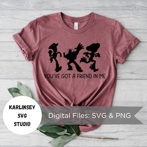 Op de afbeelding: Een maronkleurig T-shirt met een zwart silhouet van de Toy Story-personages Woody, Buzz Lightyear en Jessie die dansen. De tekst "You've got a friend in me" is onder de personages gedrukt. De tekst "KARLINSEY SVG STUDIO" is gedrukt in een cirkel linksonder in de afbeelding. De tekst "Digital Files: SVG & PNG" is gedrukt in een wit rechthoek rechtsonder in de afbeelding.