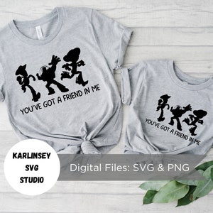 Op de afbeelding: Twee grijze T-shirts met een zwart silhouet van de Toy Story-personages Woody, Buzz Lightyear en Jessie die dansen. De tekst "You've got a friend in me" staat op de T-shirts gedrukt.