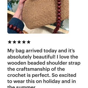 May include: A crocheted handbag with a wooden beaded shoulder strap and handle. The bag is a light brown color and has a rectangular shape. The bag is held by a person.