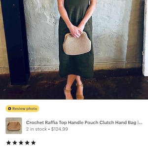 May include: A woman wearing a dark green dress holds a beige crochet raffia top handle pouch clutch hand bag. The bag is a medium size and can fit a water bottle, a wallet, and two phones.