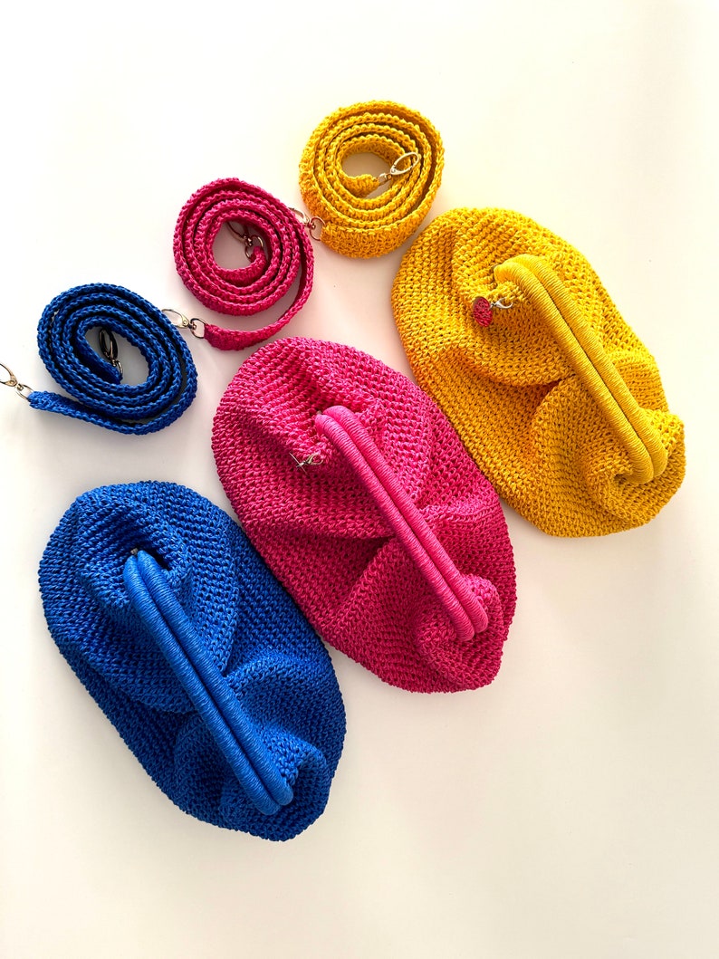 Pu&ograve; includere: Tre borse all'uncinetto in blu, rosa e giallo con tracolle abbinate. Le borse sono realizzate con una trama testurizzata e aperta e hanno una forma arrotondata leggermente cascante.