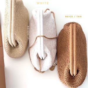 May include: Three crocheted clutch bags in light straw, white, and beige/tan. The light straw and beige/tan bags have a rounded shape with a matching handle. The white bag has a gold chain strap and a white clasp. The text "SY DESIGN" is visible.