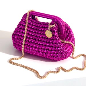 May include: A metallic fuchsia handbag with a gold chain strap. The bag has a woven texture and a curved shape with a top handle. A small gold charm with the letters "SY" hangs from the handle.