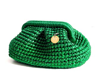 May include: A bright green clutch purse with a woven texture. The purse has a rounded shape and a clasp closure. A small gold-colored charm with the letters "SY" hangs from the side. The bag is made of a shiny, metallic material.