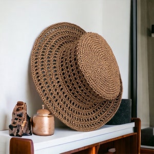 May include: A large, brown, crocheted sun hat with a wide brim. The hat is made of a natural fibre and has a delicate, open weave.