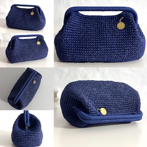 May include: A navy blue crochet handbag with a structured frame and a top handle. The bag features a gold-colored charm and a clasp closure. The crochet pattern is visible throughout the bag's exterior.