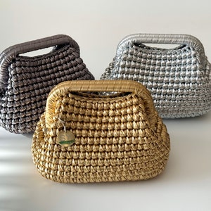 Puede incluir: Tres bolsos de crochet en dorado, plateado y gris. Los bolsos tienen una forma redondeada única y un asa superior.