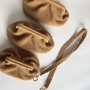 May include: Three tan woven clutch bags with a matching shoulder strap. The bags have a rounded shape with a kiss-lock closure. The strap is attached with gold-coloured metal rings.
