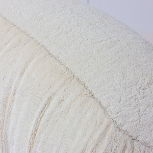 May include: Close-up of a textured, off-white cushion. The cushion has a soft, plush appearance with a series of curved, stitched lines running along its surface. The fabric has a slightly uneven texture, adding to its cozy look.