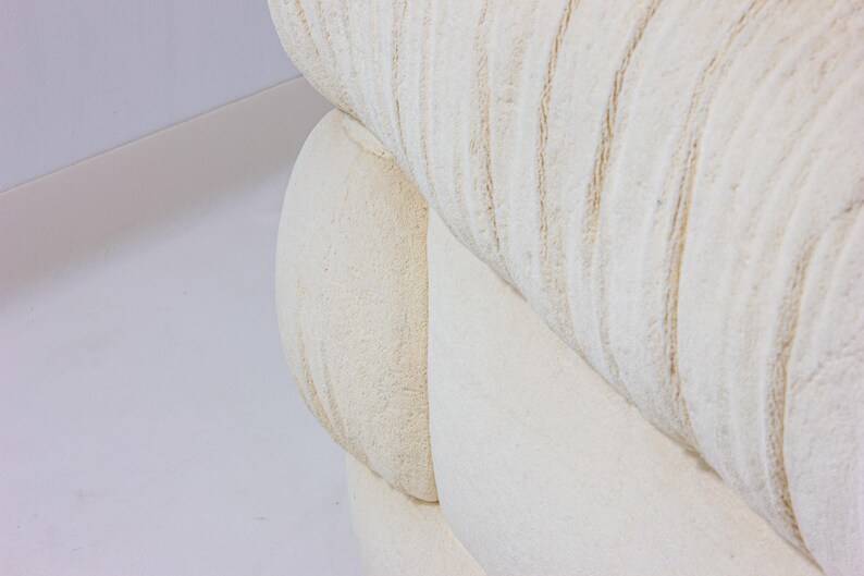 May include: Close-up of a section of a cream-coloured, textured sofa. The fabric has a ribbed pattern with subtle variations in tone. The design suggests a focus on comfort and a neutral aesthetic, suitable for various interior styles.