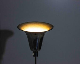 May include: A black metal floor lamp with a wide, trumpet-shaped shade. The shade is lit from within, casting a warm glow.