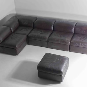 May include: A dark brown leather sectional sofa with a matching ottoman. The sofa is made up of multiple modular pieces that can be arranged in different configurations.