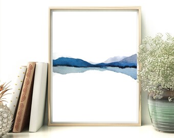 Pode incluir: Uma pintura de aquarela emoldurada de uma cordilheira azul refletida em um corpo de água. A pintura está sobre um fundo branco e é emoldurada em uma moldura de madeira clara.