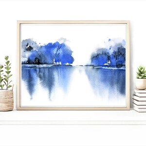Op de afbeelding: Een ingelijst aquarel schilderij van een blauw landschap met bomen die in het water worden weerspiegeld.