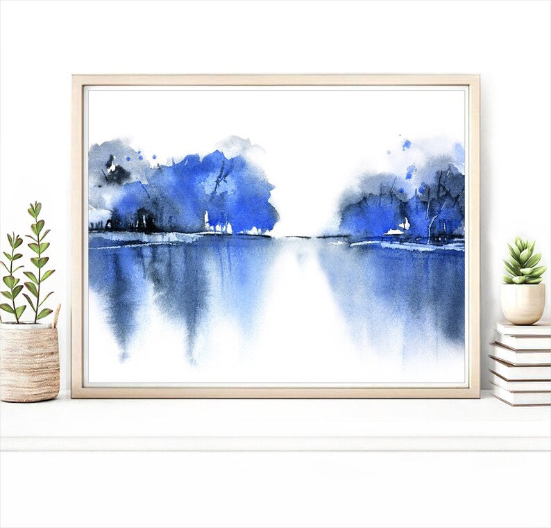 Op de afbeelding: Een ingelijst aquarel schilderij van een blauw landschap met bomen die in het water worden weerspiegeld.