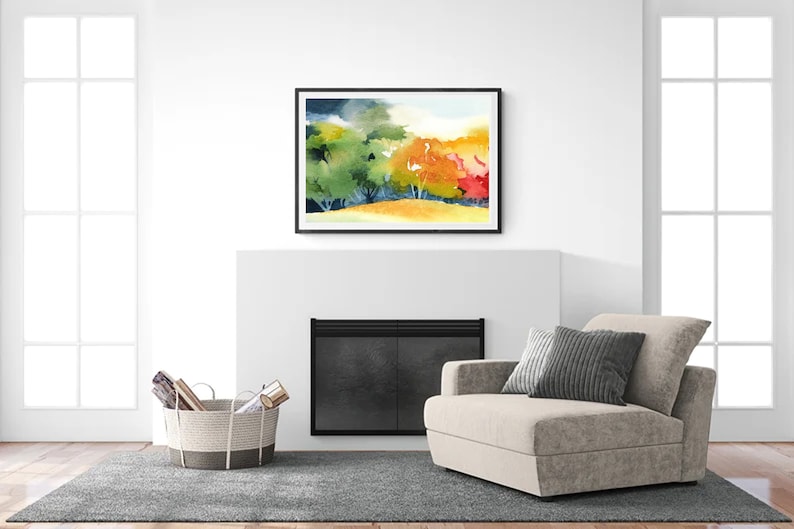 May include: A watercolor painting of a forest scene with green, yellow, orange, and red trees. The painting is framed in black and hanging above a fireplace in a living room.