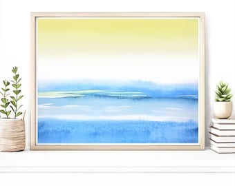 Pode incluir: Uma pintura em aquarela emoldurada com um gradiente de tons de amarelo a azul, retratando uma paisagem serena. A obra de arte está em uma moldura de madeira clara e repousa sobre uma superfície branca, com plantas em ambos os lados.
