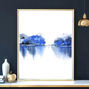 Op de afbeelding: Abstracte aquarelverf van een blauw landschap met bomen die in het water worden weerspiegeld. Het schilderij is ingelijst in goud en heeft een witte achtergrond.