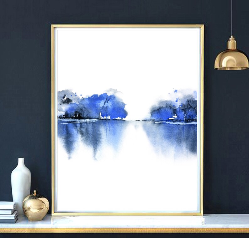 Op de afbeelding: Abstracte aquarelverf van een blauw landschap met bomen die in het water worden weerspiegeld. Het schilderij is ingelijst in goud en heeft een witte achtergrond.