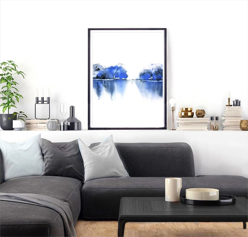 Op de afbeelding: Een ingelijst aquarel schilderij van een blauw landschap met een reflectie in het water. Het schilderij is op een witte achtergrond en is ingelijst in zwart.