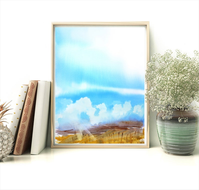 May include: A watercolor painting of a landscape with a blue sky, white clouds, and a field of tall grass. The painting is framed in a light wood frame.