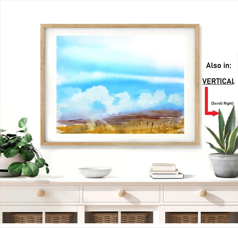 May include: A framed watercolor painting of a landscape with a blue sky, white clouds, and a field of tall grass. The painting is in a light wood frame and is hanging on a white wall.