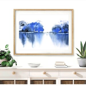 Op de afbeelding: Een ingelijst aquarel schilderij van een blauw en grijs landschap met een reflectie van de bomen in het water.