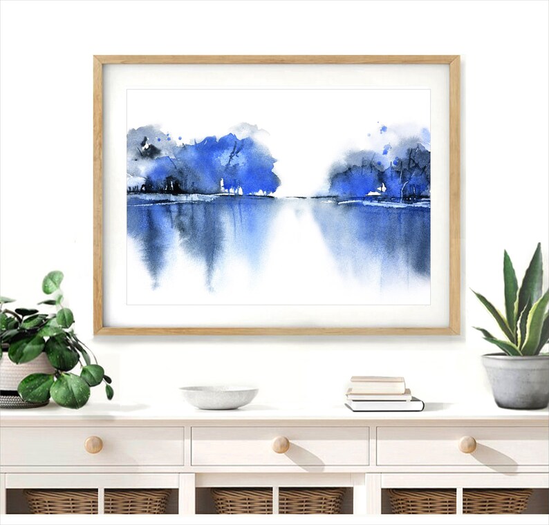 Op de afbeelding: Een ingelijst aquarel schilderij van een blauw en grijs landschap met een reflectie van de bomen in het water.